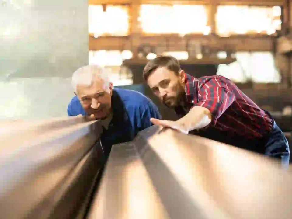 Dois homens inspecionando uma peça metálica em uma fábrica, com atenção aos detalhes e à qualidade da superfície do material.