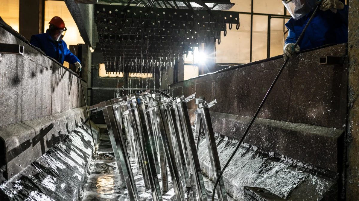 Trabalhadores realizando tratamento térmico em peças de aço mergulhadas em banho de resfriamento em indústria metalúrgica