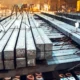 Close-up de barras quadradas de aço recém-produzidas e empilhadas, com marcações numéricas, em uma indústria metalúrgica.